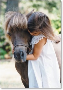 Girl in white dress hugs brown pony