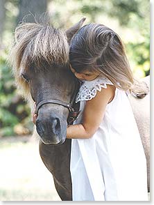 Girl in white dress hugs brown pony