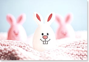 a toy easter egg with bunny ears and a big toothy smile sits on a blanket